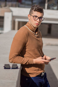 Portrait of man using mobile phone by retaining wall