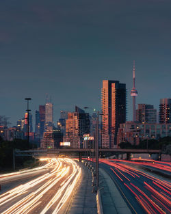 Light trails on road amidst buildings against sky in city