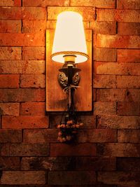 Low angle view of illuminated lamp hanging against brick wall