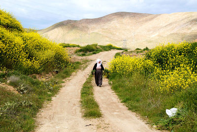Woman holding plants while walking on dirt road