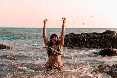 Woman splashing water in sea against clear sky at sunset