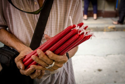 Midsection of man selling red candles on street in city