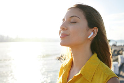 Woman breathing with closed eyes listening relaxing music with earphones on city bay at sunset