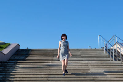 Low angle view of woman standing on staircase against blue sky