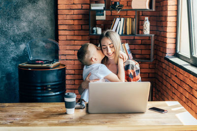 Son hugs mother working on laptop. family bonding, mom and son use laptop for learning.