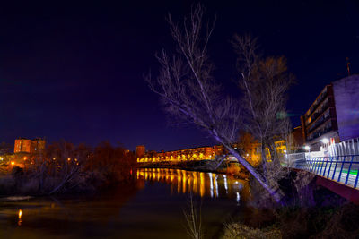 Illuminated bridge over river against sky at night