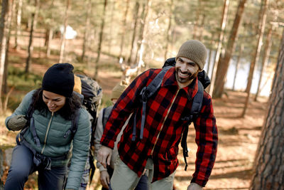 Happy man wearing plaid shirt while hiking with female friend in forest