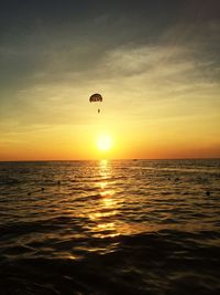 Parachute over sea against orange sky