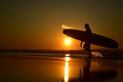 Surface level of silhouette man with surfboard walking on shore during sunset