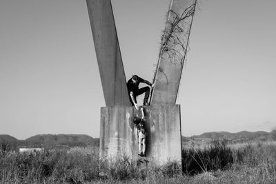 Father assisting daughter hanging on column at grassy field