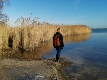 Rear view of man standing by lake against sky