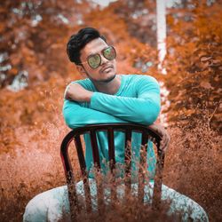 Young man sitting on chair against trees during autumn