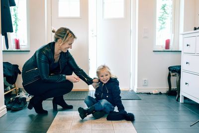 Smiling mother crouching while daughter with knit hat sitting at home