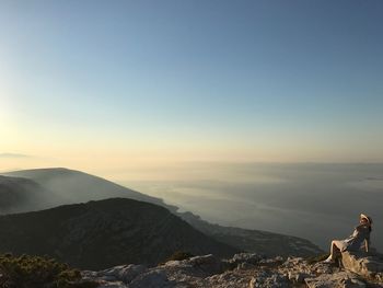 Woman sitting on mountain against sky during sunset