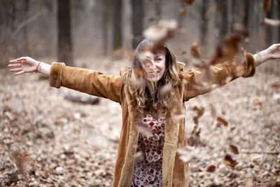 Cheerful young woman enjoying with autumn leaves on field