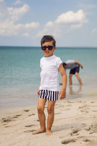 Portrait of a boy child in sunglasses stands on the beach in summer