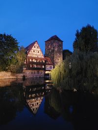 Buildings by lake against clear blue sky