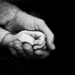 Cropped hands of man and baby against black background