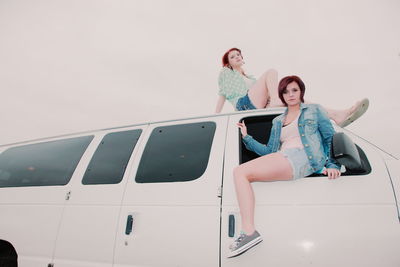 Low angle view of friends sitting on van against clear sky