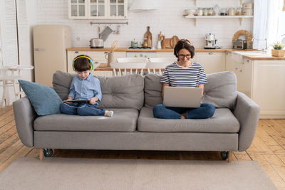 Full length of young woman using phone while sitting on sofa