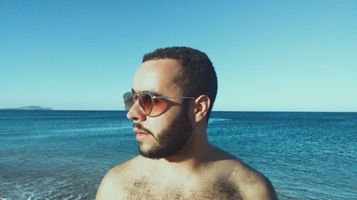 Close-up of young man wearing sunglasses at beach against clear sky