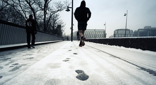 Rear view of man walking on snow in city