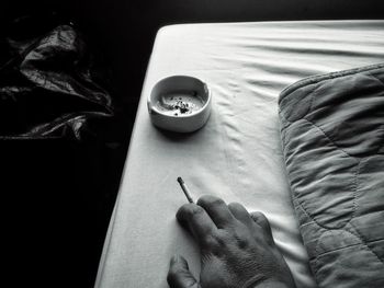 Cropped hand of man smoking cigarette on bed at home