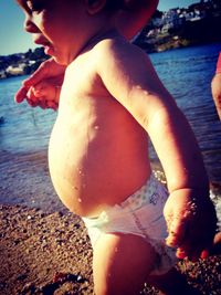 Midsection of shirtless boy at beach