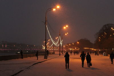 People walking on illuminated street in city at night