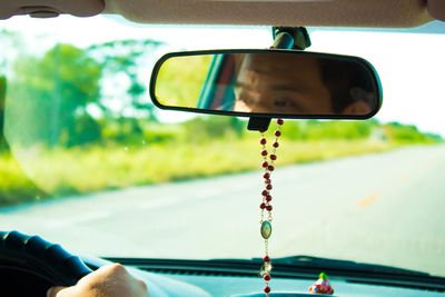 Reflection of man driving car on rear-view mirror