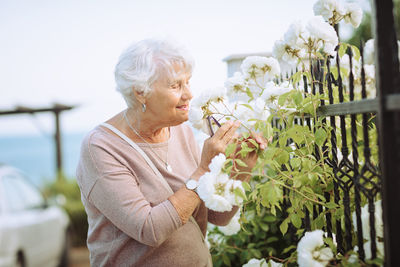 Elderly woman admiring beautiful bushes with colorful roses.