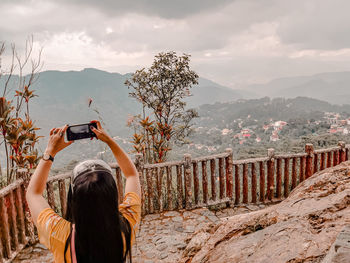 Rear view of man photographing on mountain against sky