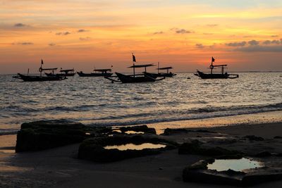 Silhouette boats moored on sea against orange sky