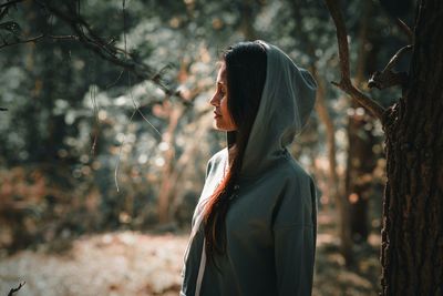 Woman wearing hooded shirt while standing against tree