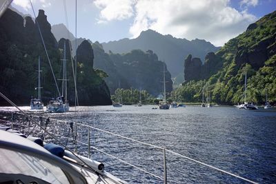 Boats sailing in river against rocky mountains during sunny day