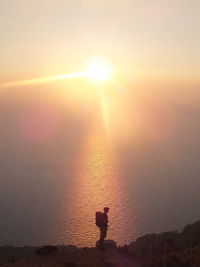 Silhouette person standing in sea against sky during sunset