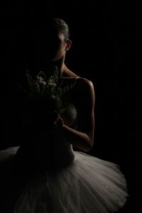 Ballet dancer holding flowers against black background