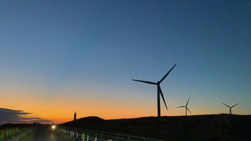 Wind turbines on land against sky during sunset