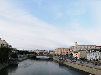 Bridge over river by buildings in city against sky