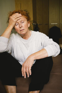 Worried elderly woman sitting with head in hand at home