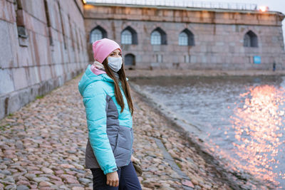 A woman walks in the city by the river in a protective mask