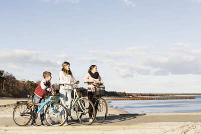 Full length of happy friends with bicycles at beach