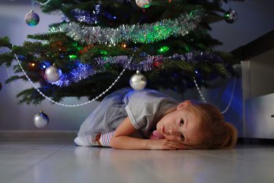 Portrait of girl lying down on floor by christmas tree