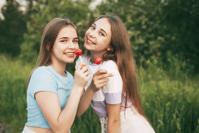 Portrait of smiling friends holding lollipops standing against plants in park