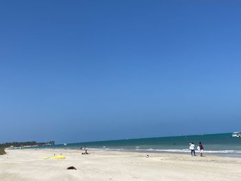 People on beach against clear blue sky