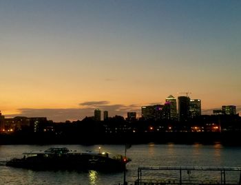 Illuminated buildings by river against sky during sunset