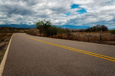 Empty road amidst field against cloudy sky