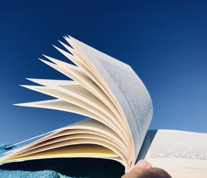 Close-up of hand holding book against blue sky