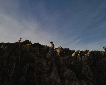 Low angle view of man sitting on rock formation against sky