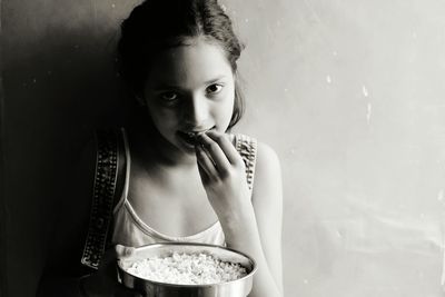 Portrait of girl eating food against wall at home